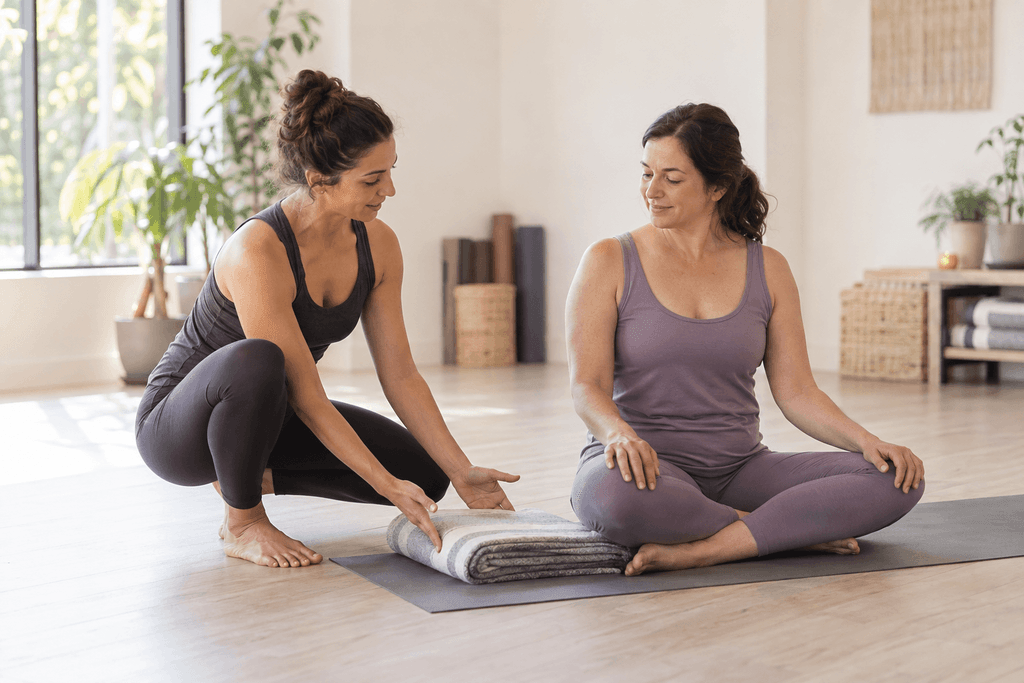 Insegnante di yoga accanto a una principiante seduta sul tappetino durante una lezione